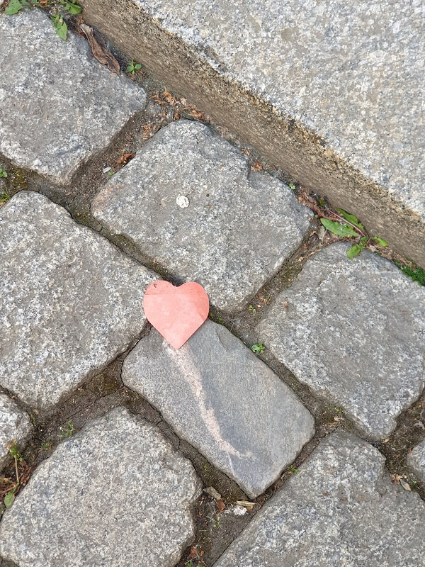 Ein kleines, rotes Papierherz liegt auf grauem Kopfsteinpflaster neben einer Steinstufe. Passend zum Blogbeitrag über Authentizität und Veränderung.